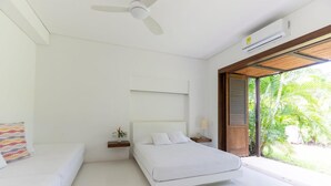 Un dormitorio moderno con cama, ventilador de techo, equipo de aire acondicionado, mesita de noche con lámpara y vistas a zonas verdes.