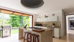 Una cocina moderna con una isla central, taburetes de bar, una parrilla empotrada y vistas a un jardín exuberante.