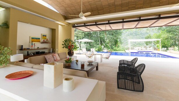 Amplia sala de estar con ventilador de techo, sofá, una mesa de centro y vista a una piscina.