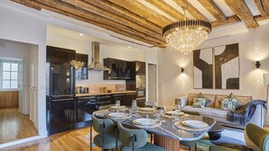 Une cuisine moderne avec un coin repas, des poutres apparentes en bois au plafond et un lustre.