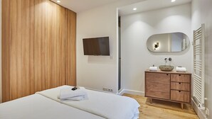 Une chambre moderne avec une tête de lit en bois, un téléviseur à écran plat, une coiffeuse en bois avec un miroir et un radiateur.
