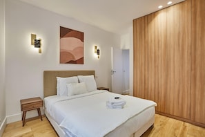 A modern bedroom with a large bed, a wooden wardrobe, and a wall-mounted artwork.
