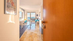 A hallway leading to a dining area with a table and chairs, a sofa, and a window with a view. - Sky & Sea Apartment by Wonderful Italy (Ospedaletti)