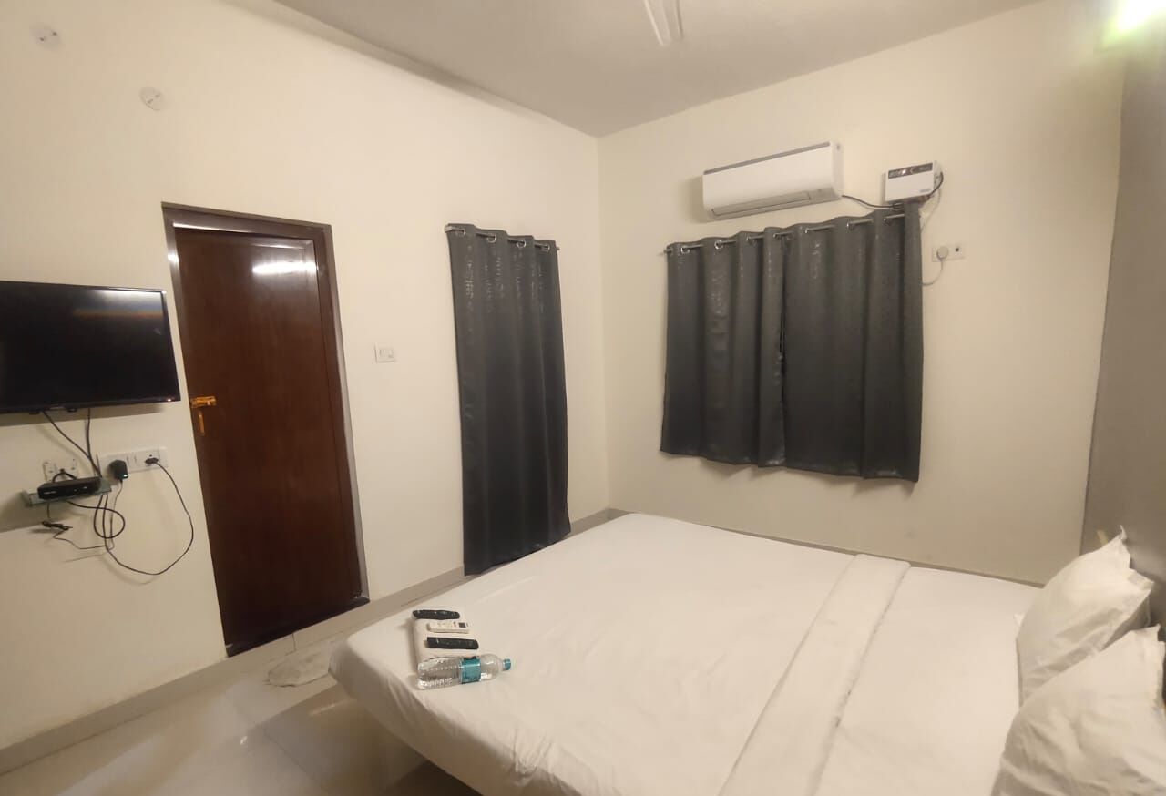 A bedroom with a bed, a TV mounted on the wall, an air conditioning unit, and a door.