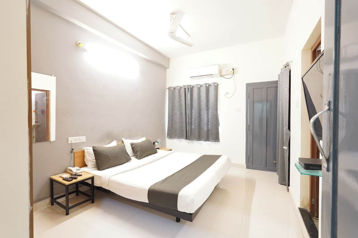 Una habitación de hotel moderna con una cama, mesita de noche, lámpara y televisión montada en la pared.