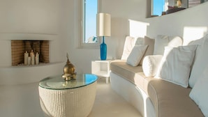 A modern living room with a beige sofa, a glass coffee table, a blue lamp, and a fireplace with candles. - Elegant Villa With View (Mykonos)