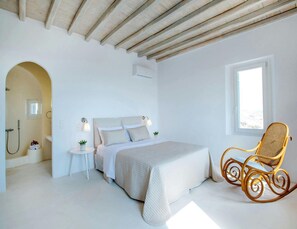 A bedroom with a bed, a rocking chair, a small table, and a window.