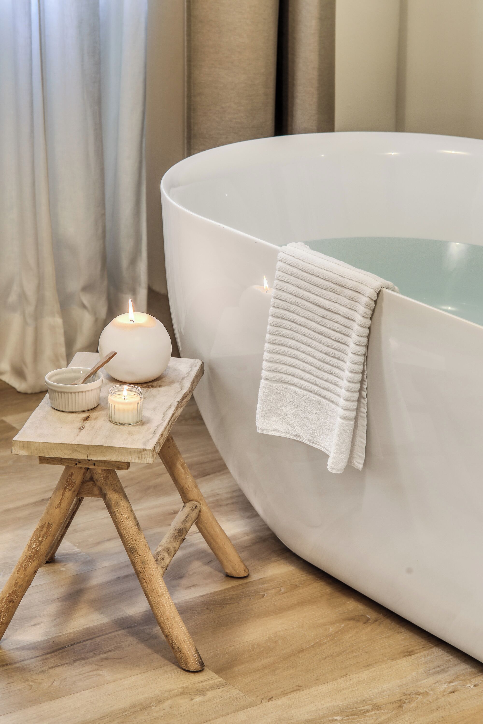 Et spabad med et hvidt håndklæde, et tændt stearinlys og en lille skål med en ske på en træskammel.