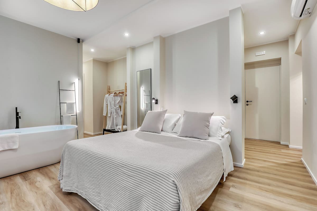 A modern bedroom with a large bed, a bathtub, and a walk-in closet.