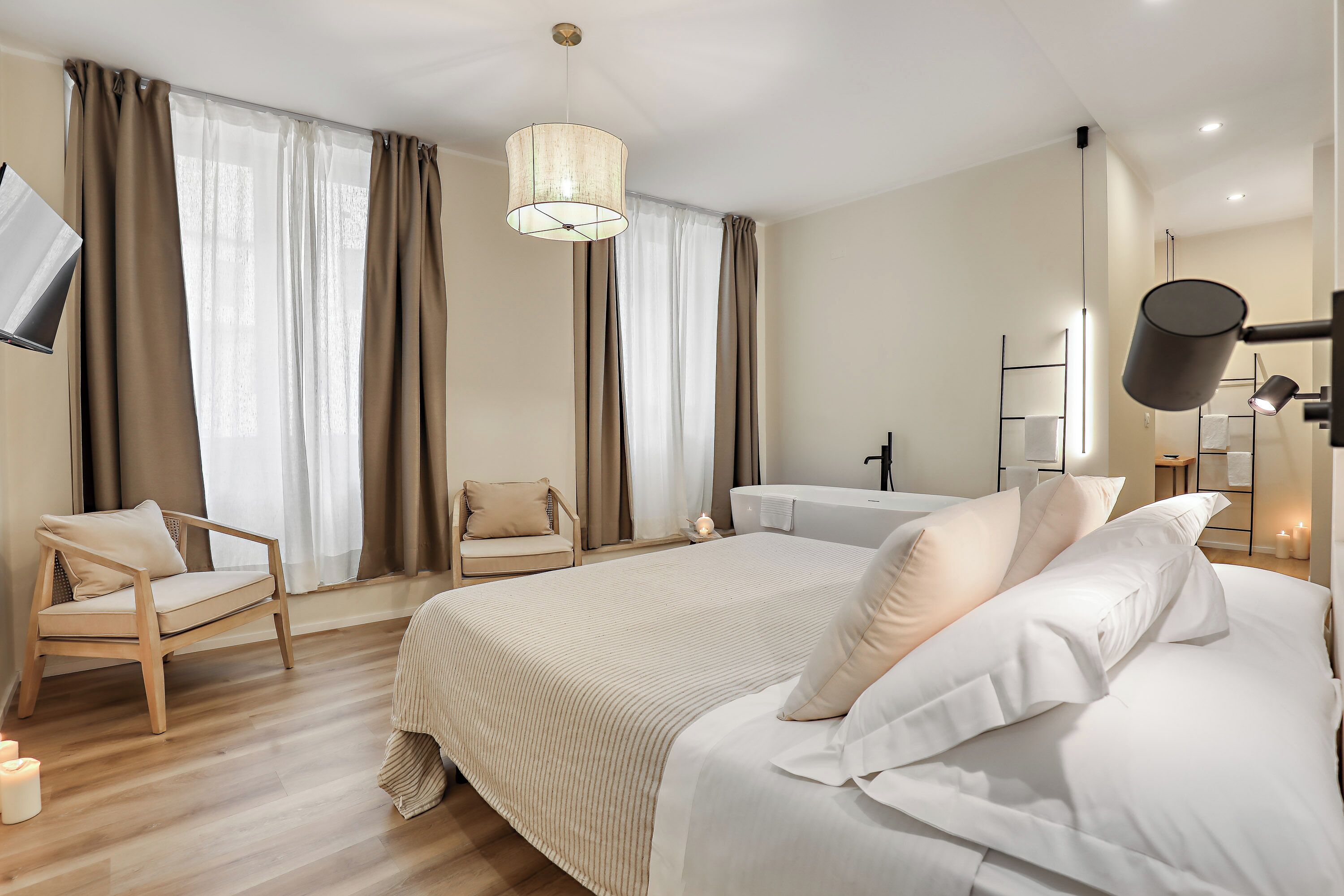 Een moderne hotelkamer met een groot bed, een fauteuil, een bureau en een aan de muur bevestigde televisie.