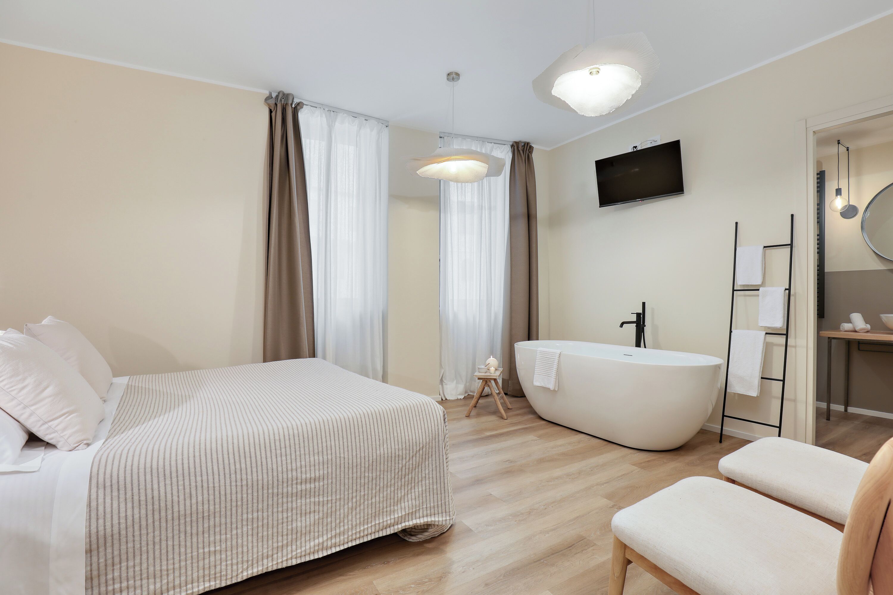 Une chambre moderne dotée d’un grand lit, d’un coin salon, d’une baignoire et d’un téléviseur fixé au mur.