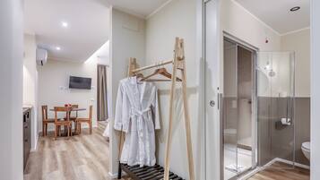 A hotel room with a wooden floor, a dining area with a table and chairs, a TV mounted on the wall, and a glass shower enclosure.