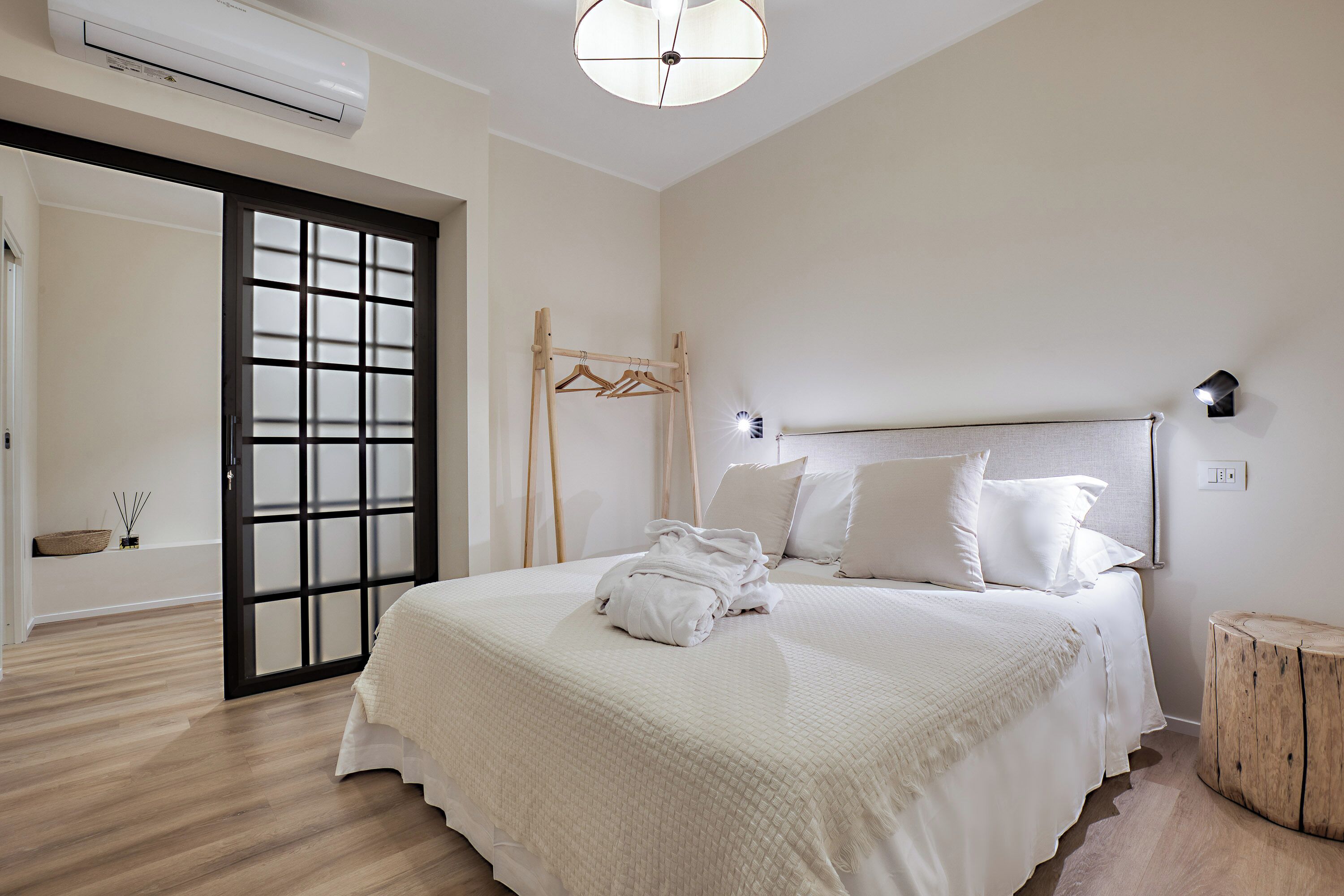 A bedroom with a bed, a wooden side table, a hanging wooden rack, and a sliding glass door.