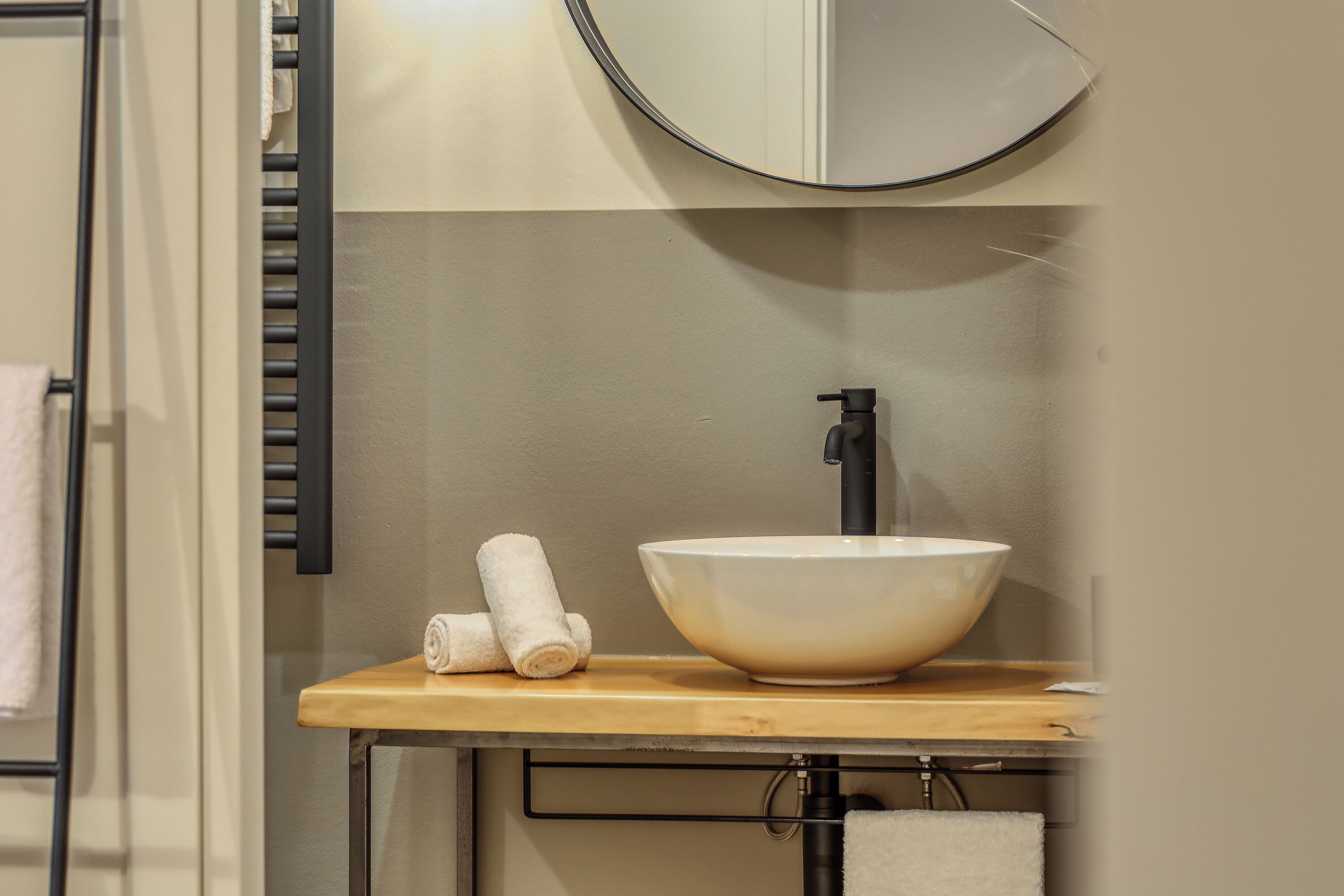 A bathroom with a wooden vanity, a white sink, and a round mirror.