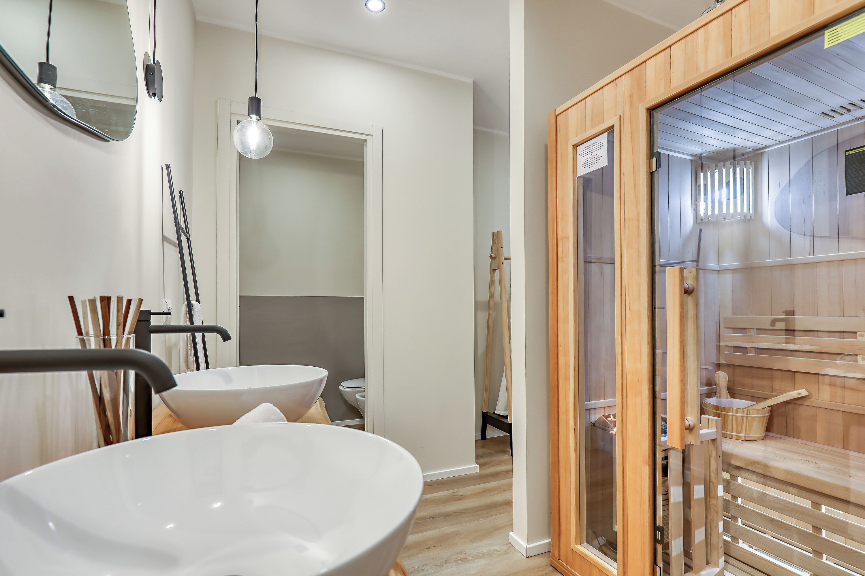 Un baño moderno con un lavabo blanco grande, un espejo y una zona de sauna de madera.
