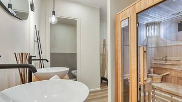 Un baño moderno con un lavabo blanco grande, un espejo y una zona de sauna de madera.