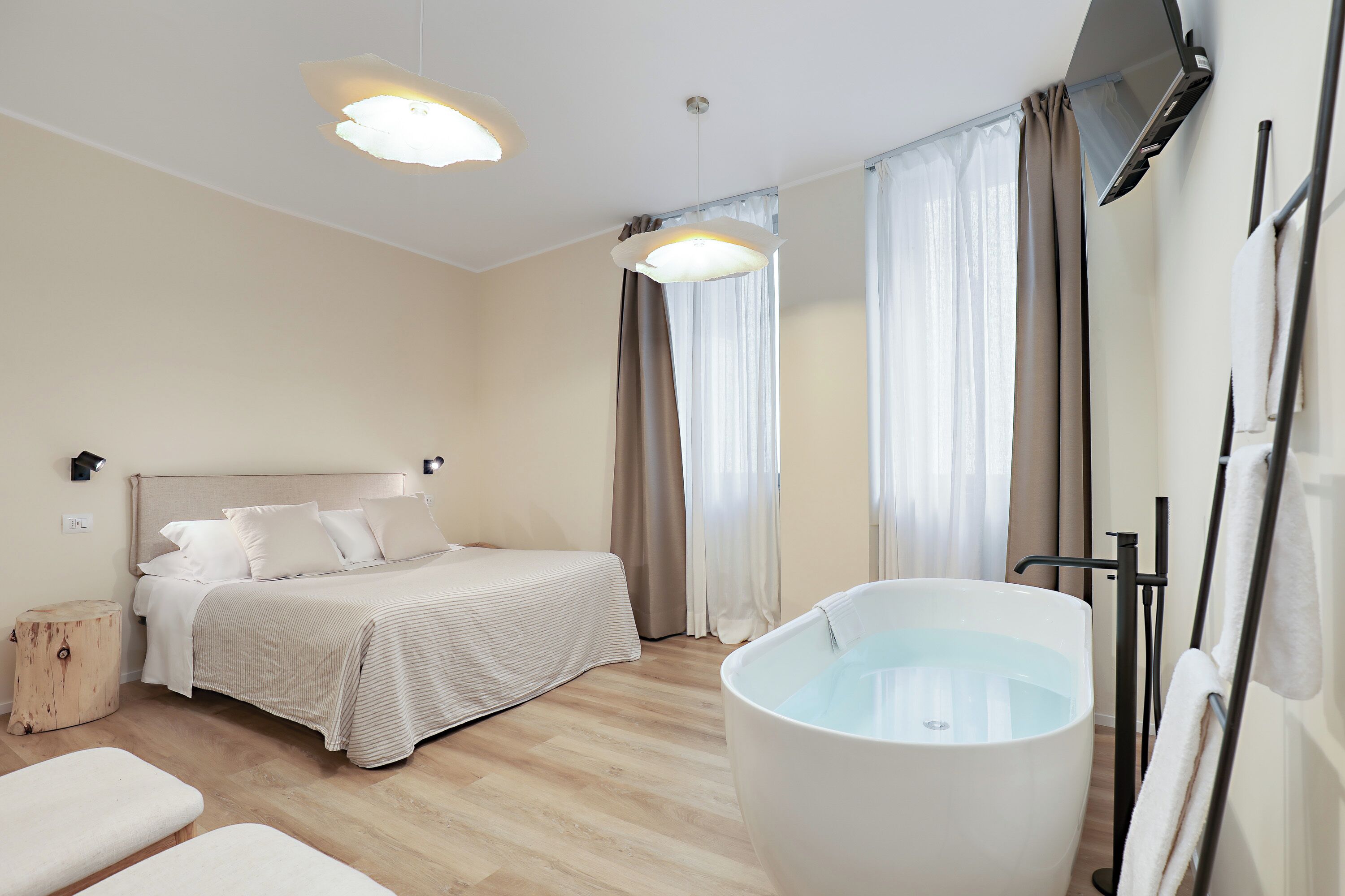 A modern hotel room with a large bed, a bathtub, and a wooden floor.