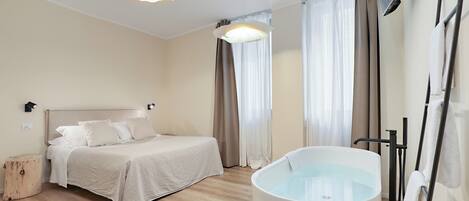 A modern hotel room with a large bed, a bathtub, and a wooden floor.