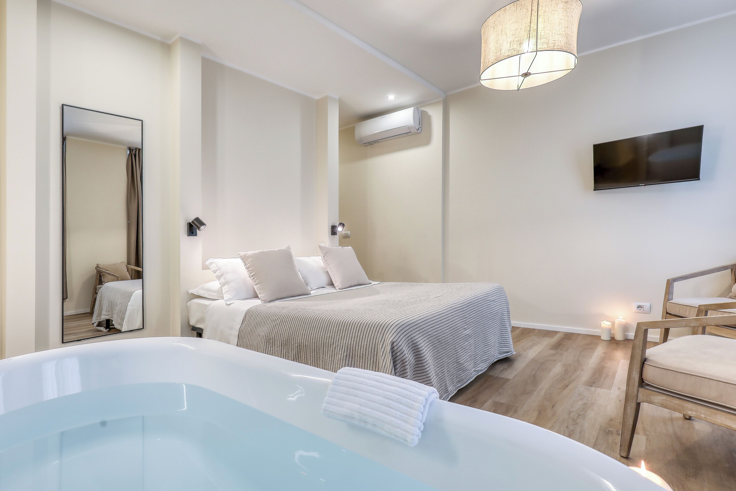 Une chambre moderne avec un grand lit, un coin salon avec un fauteuil, une baignoire, un téléviseur à écran plat et un miroir.