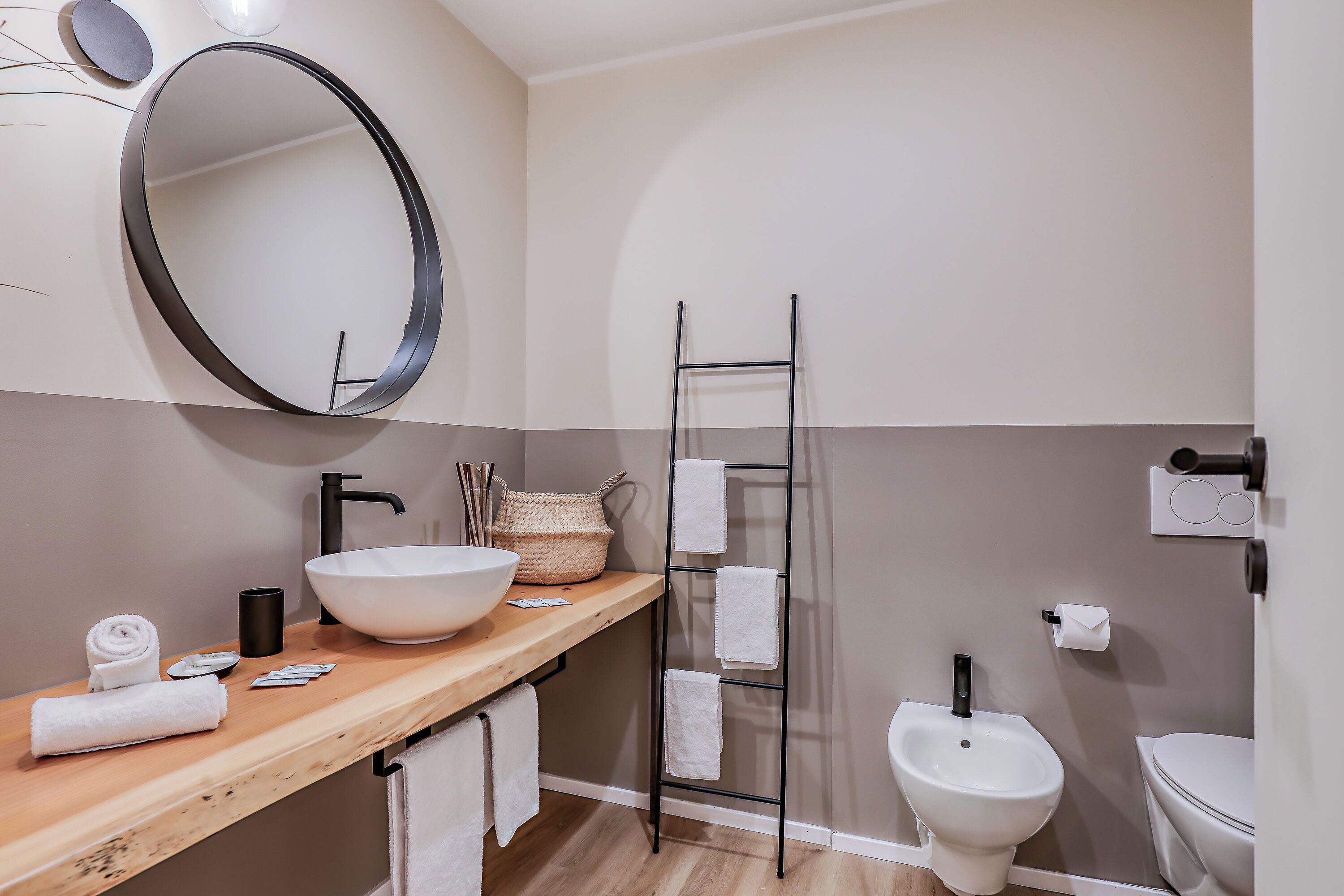 Un baño moderno con tocador de madera, un espejo grande, un lavabo blanco, un bidé y un perchero para toallas.
