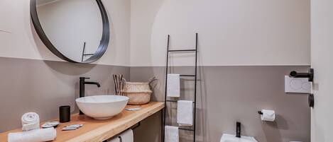 Un baño moderno con tocador de madera, un espejo grande, un lavabo blanco, un bidé y un perchero para toallas.