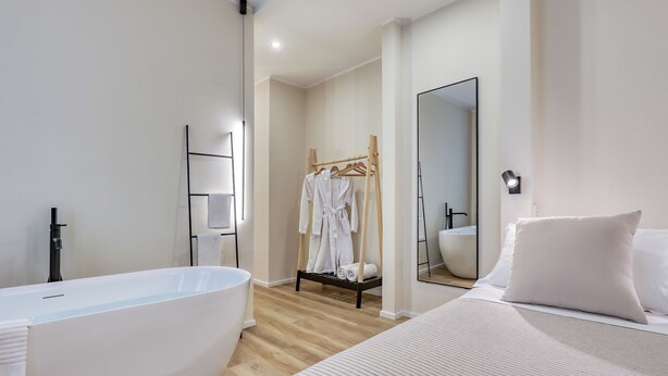 A modern bathroom with a freestanding bathtub, a wooden robe rack, and a large mirror. - Welchome suites (Perugia)
