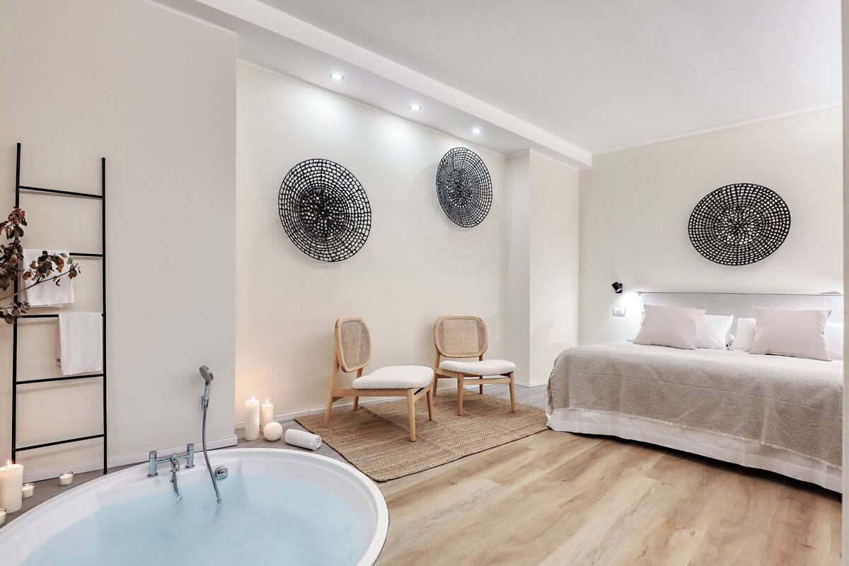 A modern bathroom with a bathtub, two chairs, a bed, and decorative wall art.