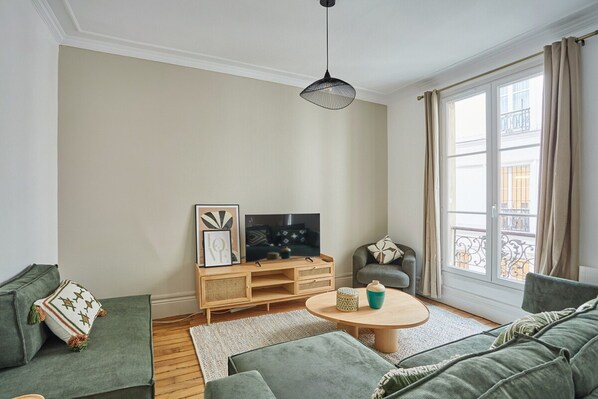 A modern living room with a sofa set, a coffee table, a TV, and a large window with curtains. - Sublim Apartment Beaubourg/le Marais (Paris)