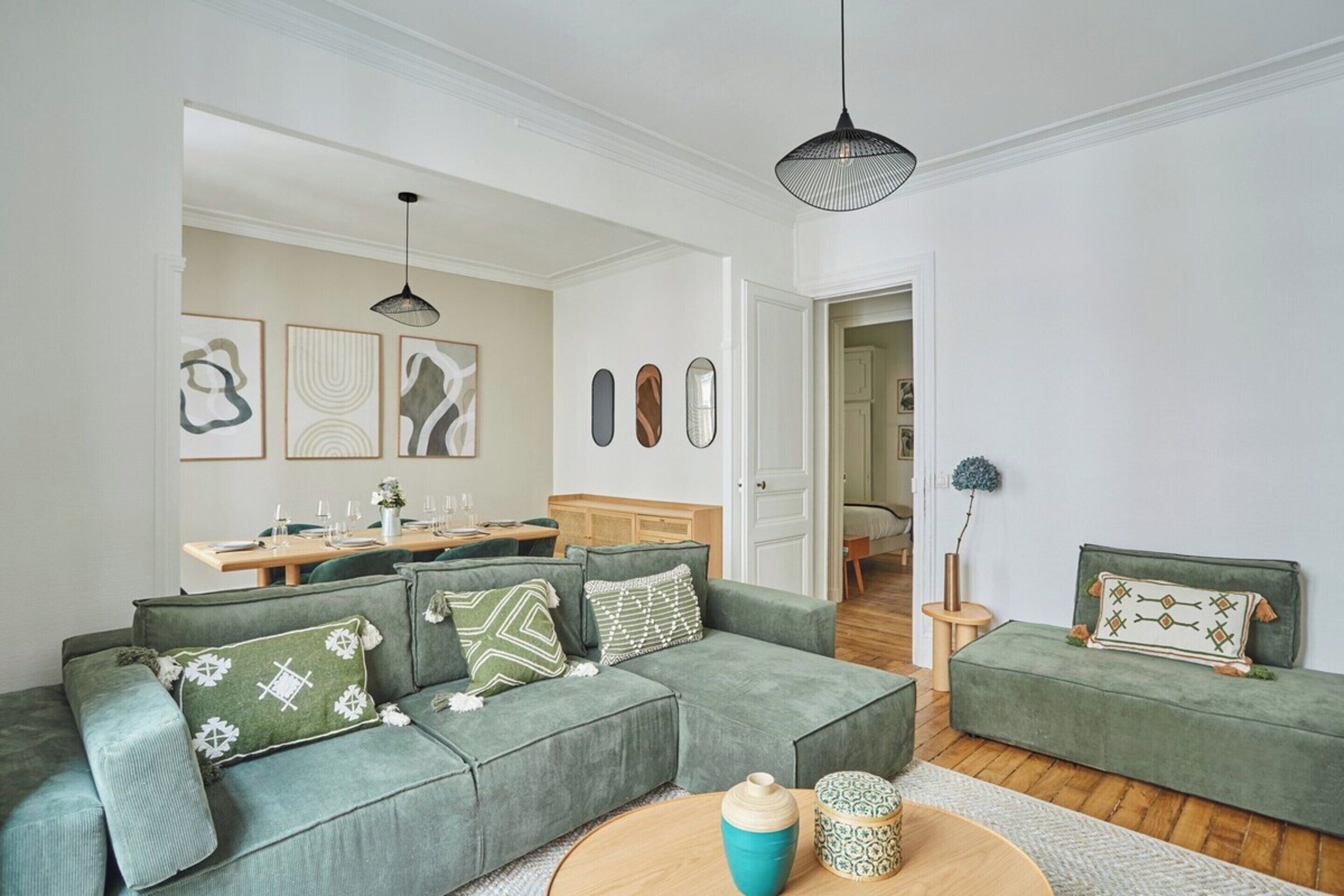 A modern living room with a green sofa set, a wooden coffee table, and a dining area with a wooden table and chairs.