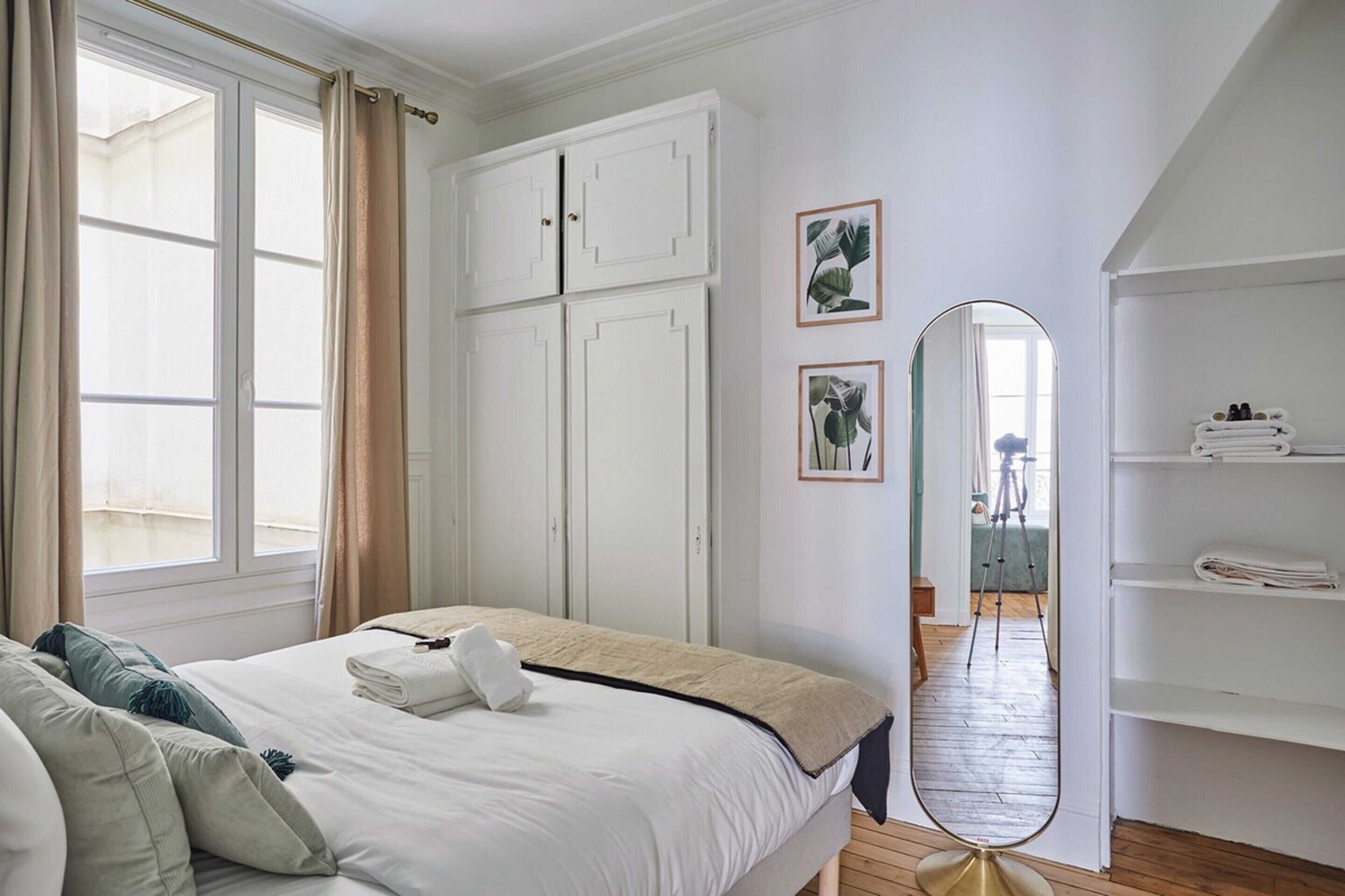 A bedroom with a bed, a wardrobe, a mirror, and a window with curtains.