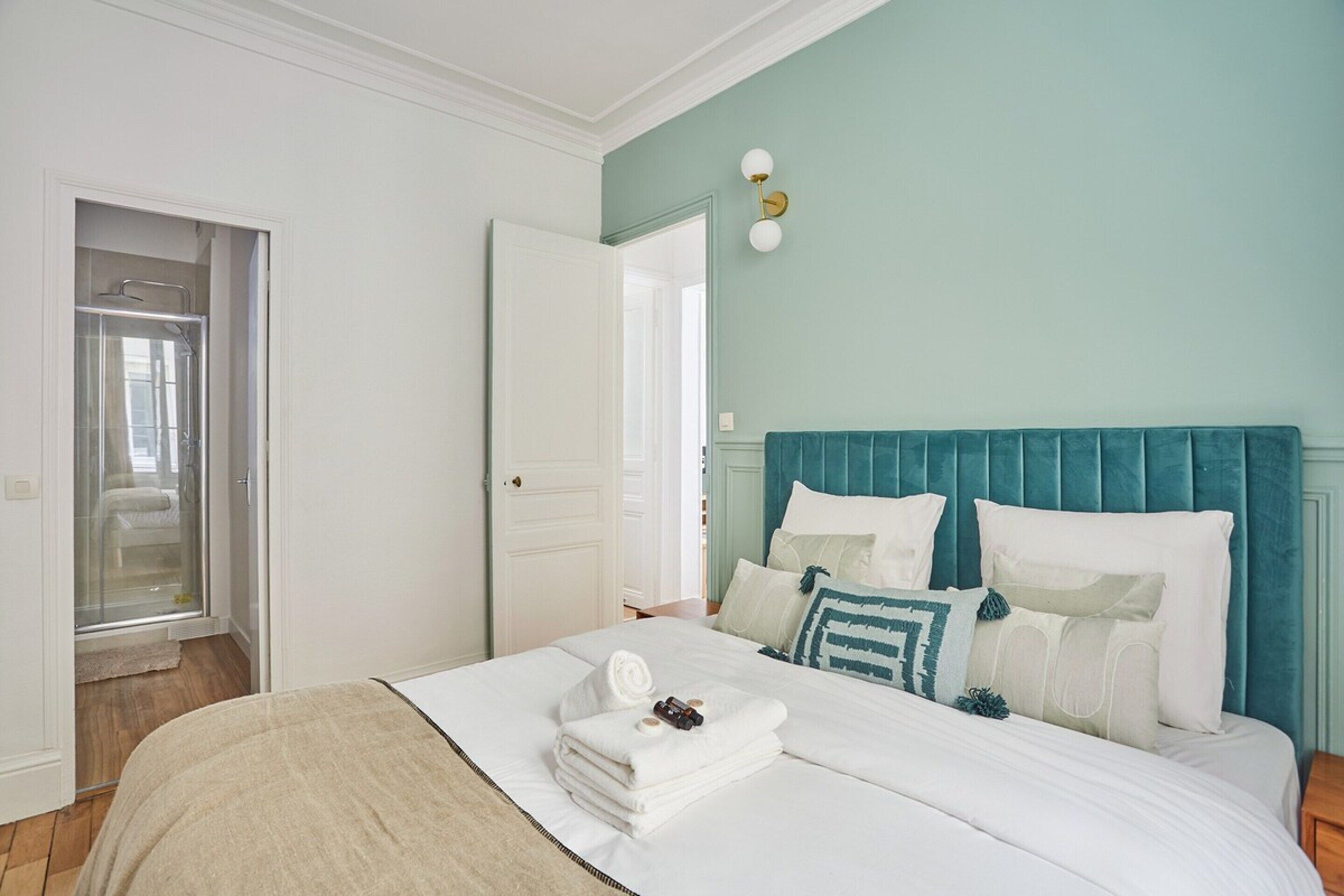 A bedroom with a bed, a nightstand, a window, and a door leading to a bathroom.
