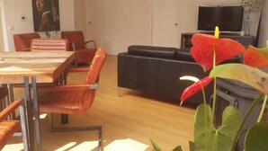 Un área de comedor con una mesa y sillas de madera, un sofá negro y un televisor sobre un mueble.