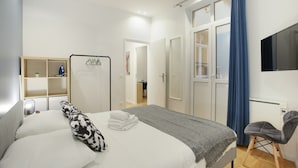 Quarto de hotel com cama, uma cadeira, televisão e guarda-roupa.