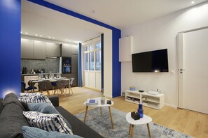 A modern living room with a grey sofa, a coffee table, and a dining area with chairs and a table. A flat-screen TV is mounted on the wall, and there is a white cabinet below it. - New Apartment Center of Paris (Paris)
