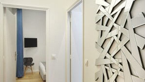 Um corredor com design moderno na parede, uma TV de tela plana fixada na parede, uma cadeira e uma cama ao fundo.