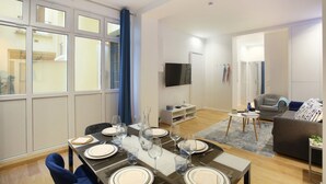 Uma sala de estar moderna com área de jantar, janelas amplas, televisão de tela plana e sofá cinza.