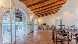 A spacious dining area with a high ceiling and a thatched roof, featuring a long wooden table and chairs, and a television on a stand. - Villa Laura by Wonderful Italy (Alghero)