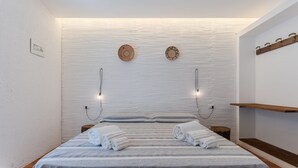 A neatly made bed with striped bedding and rolled towels, a wall-mounted light fixture, and a wooden shelf with hooks. - Villa Laura by Wonderful Italy (Alghero)