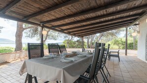 An outdoor dining area with a covered patio, a table set for four, and a view of the sea. - Villa Laura by Wonderful Italy (Alghero)