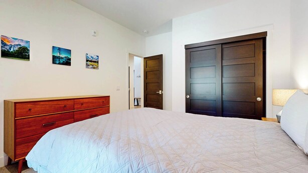 A bedroom with a bed, a wooden dresser, a dark door, and three landscape paintings on the wall.