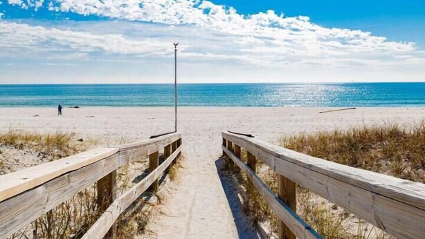 A wooden boardwalk leading to a beach with a clear sky and calm sea. - Casa Del Mar - Beautiful New Rental (Gulf Shores)