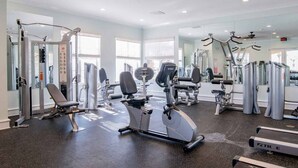 A modern gym with various exercise equipment, large windows, and a clean, spacious layout. - Casa Del Mar - Beautiful New Rental (Gulf Shores)