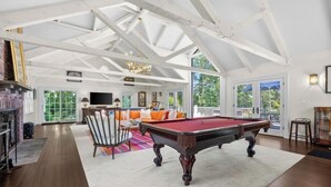 A spacious room with a pool table, a fireplace, and a large window offering a view of the outdoors. - Luxury rental with pool. Close to village and beach RPMS157 (Osterville)