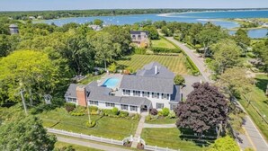 A large house with a swimming pool, surrounded by lush greenery and a lake. - Luxury rental with pool. Close to village and beach RPMS157 (Osterville)