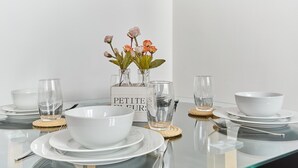 Een eettafel gedekt met witte kommen, borden en glazen, met een bloevas ernaast.