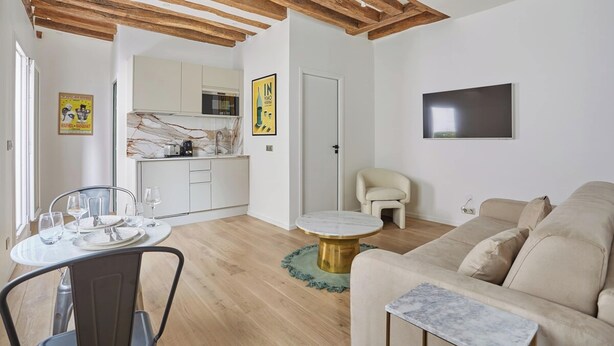 A modern living room with a beige sofa, a round coffee table, and a dining area with a white table and chairs. - Eiffel Tower Apartment/invalide (Paris)