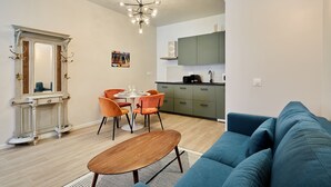 A modern living room with a blue sofa, a wooden coffee table, and a dining area with orange chairs and a white table. - Charmant Duplex 1 Chambre Centre de Paris (Paris)