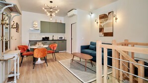 A modern living room with a sofa, a dining table with chairs, a kitchen area with cabinets, and a staircase. - Charmant Duplex 1 Chambre Centre de Paris (Paris)