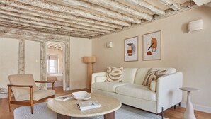 Ein Wohnzimmer mit Holzboden, einem weißen Sofa mit gemusterten Kissen, einem runden Couchtisch und einem Beistelltisch.