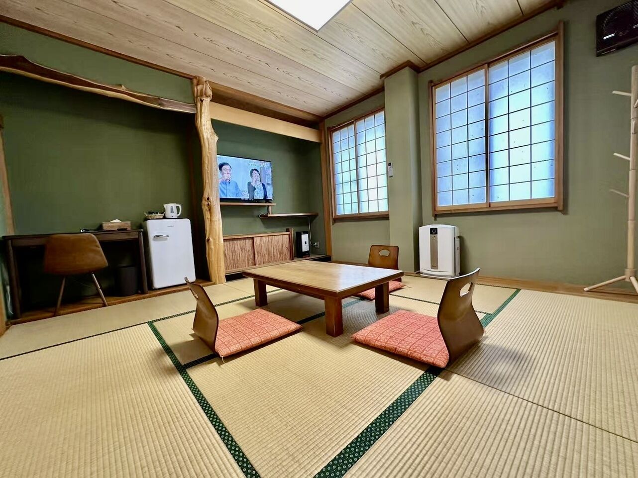 Une pièce avec un sol recouvert de tatamis, une table et des chaises en bois, un téléviseur et une fenêtre de style japonais traditionnel.